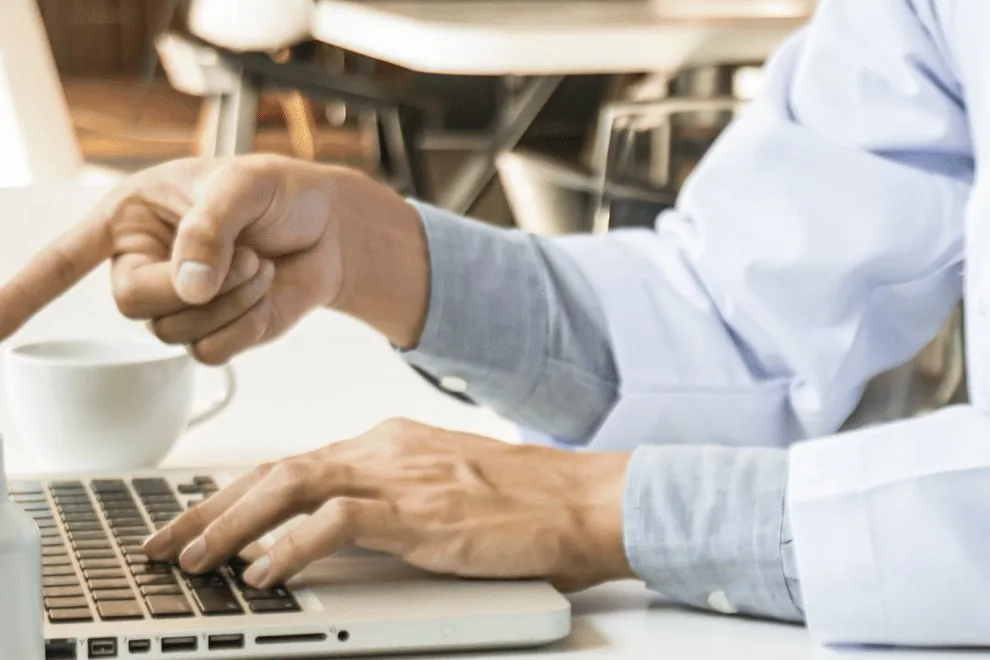 A doctor in a white coat points at a laptop screen while typing